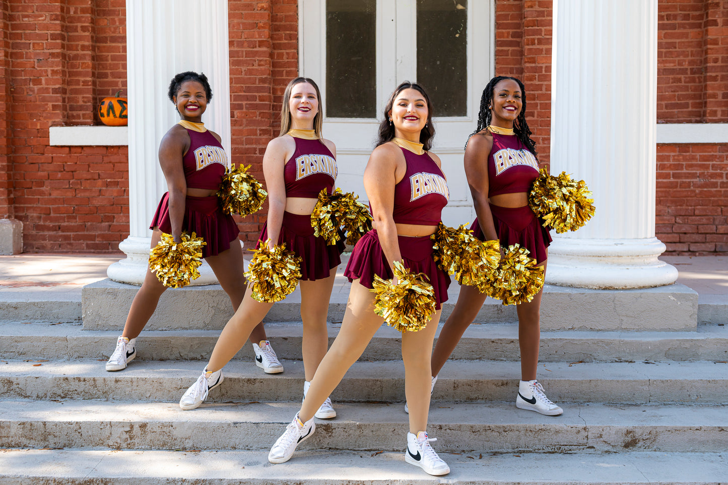 Four members of the cheer team pose on the steps of the Euphie building at Erskine