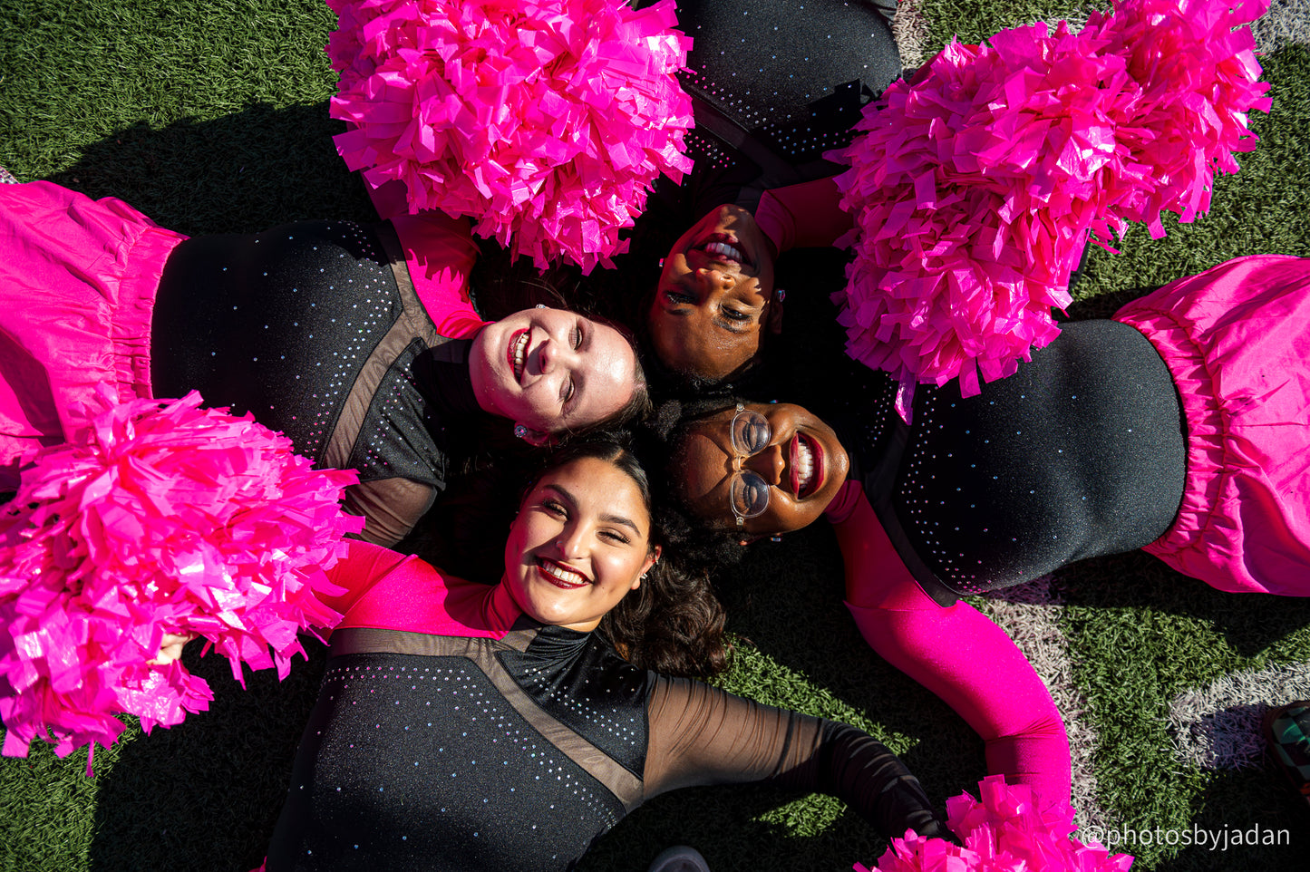 Members of the cheer team pose with pink pompoms on the football field