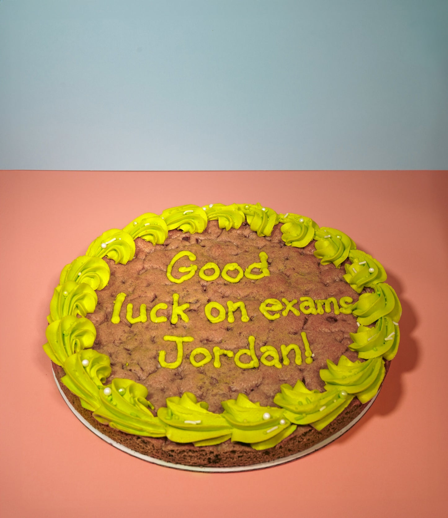 A cookie cake with green icing on the border and a message that reads "Good luck on exams Jordan!"