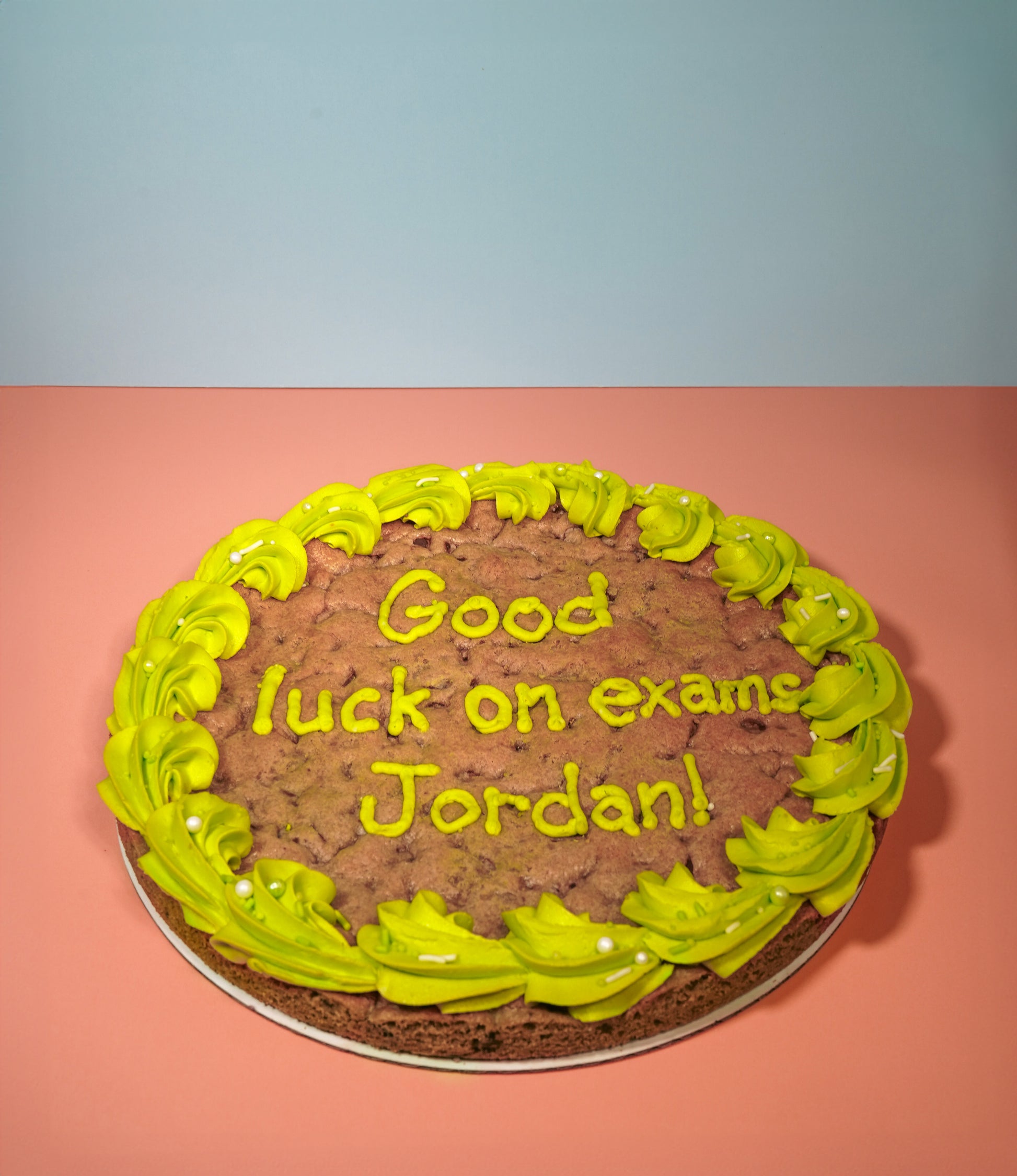 A cookie cake with green icing on the border and a message that reads "Good luck on exams Jordan!"